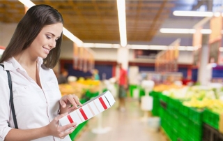 A woman reading nutrion label on a box in a grecery store.